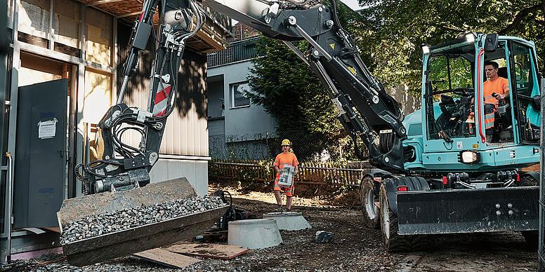 Koparka kołowa Wacker Neuson EW100 przenosząca materiały sypkie za pomocą łyżki uchylnej na placu budowy.