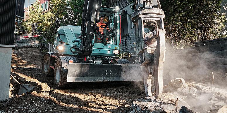 Koparka kołowa Wacker Neuson EW100 wyposażona w młot hydrauliczny podczas prac rozbiórkowych w ciasnej dzielnicy mieszkalnej.