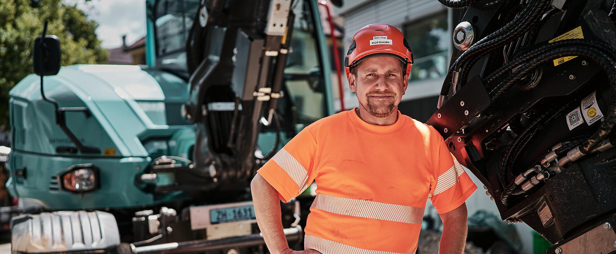 Kierowca maszyn budowlanych stoi obok koparki kołowej typu Wacker Neuson EW100, wyposażonej w hydrauliczne osprzęt dodatkowy.
