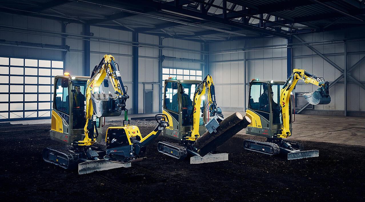 minikoparki ustawione w rzędzie w hali przemysłowej