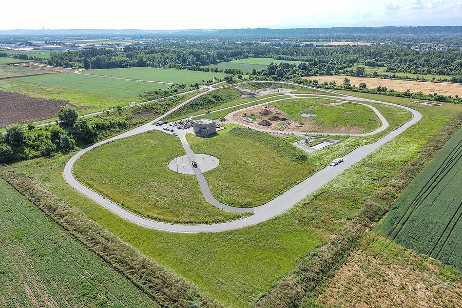 Widok z lotu ptaka na Test Arena w Linzu, na którym widać utwardzony tor okrężny, obszar do testów w trudnym terenie, stację pomiaru hałasu oraz obszary testowe położone pośród rozległego zielonego krajobrazu.