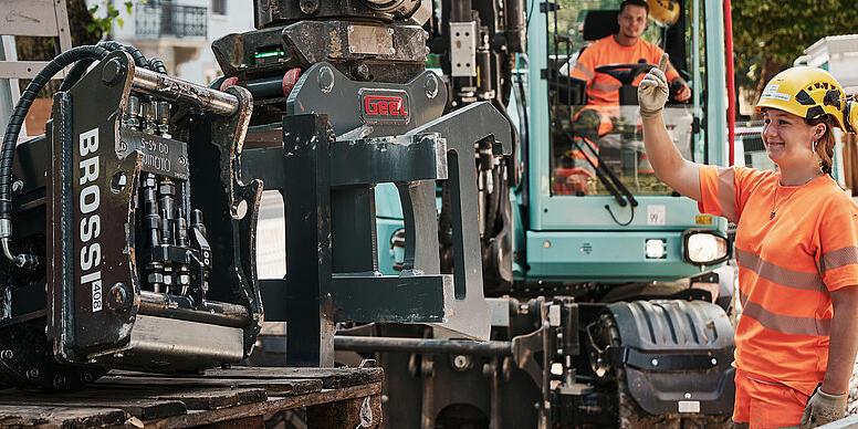 Operator przygotowujący osprzęt hydrauliczny do koparki kołowej Wacker Neuson EW100 na miejskim placu budowy.