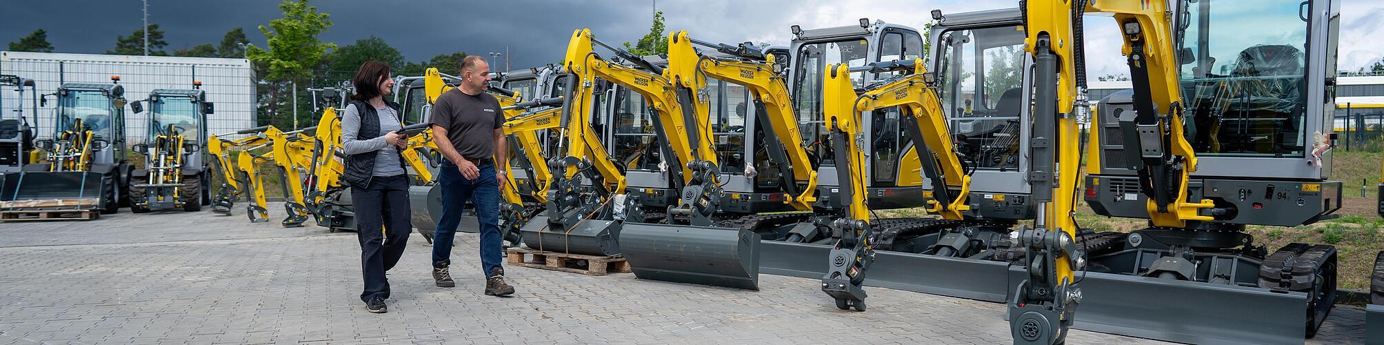 two persons walking in front of some wacker neuson excavators