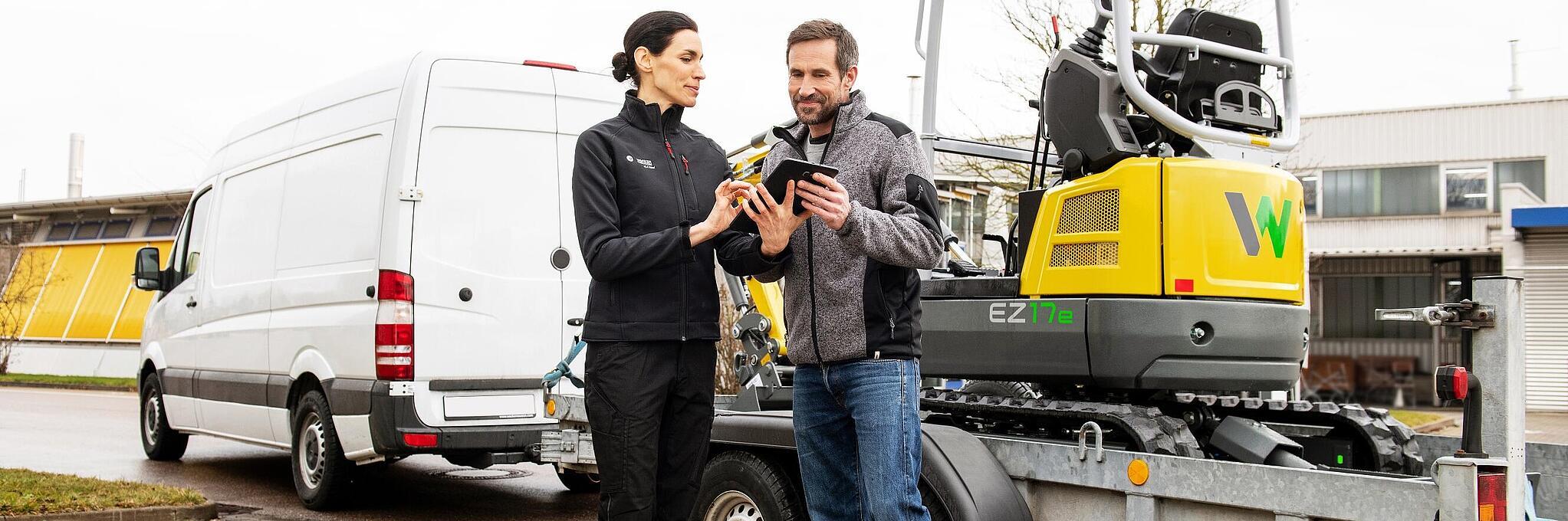 Wacker Neuson employee and customer in front of zero emission tracked excavator concluding a rental contract.