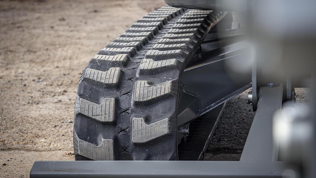 Zbliżenie gumowej gąsienicy na piaszczystym podłożu.