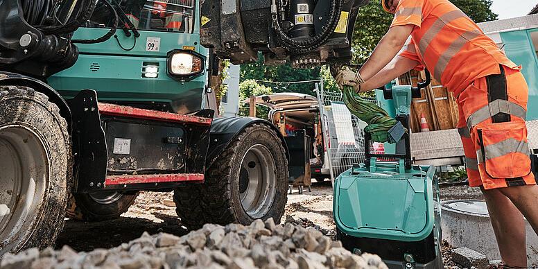 Operator wymienia osprzęt w koparce kołowej Wacker Neuson EW100 podczas prac na placu budowy.